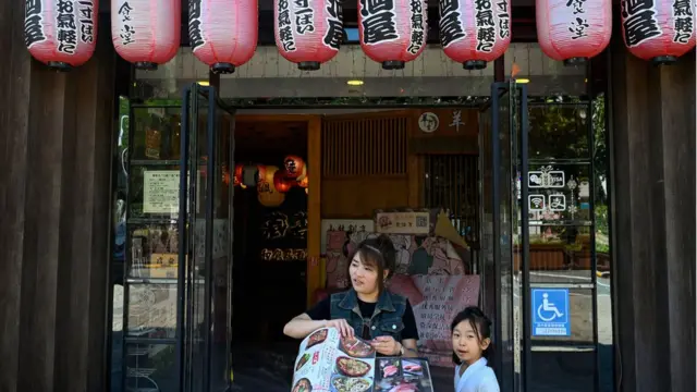 A worker displays the menu of a Japanese restaurant near the Japanese embassy in Beijing on August 29. 2023. Chinese sushi and sashimi lovers have expressed reservations after Japan kicked off plans for the disposal of waste from the stricken power plant into the Pacific Ocean, 12 years after one of the world's worst nuclear disasters. (Photo by Pedro PARDO / AFP) (Photo by PEDRO PARDO/AFP via Getty Images)