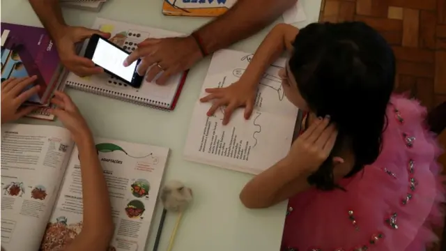 Niños haciendo deberes con un celular en medio