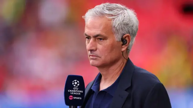 Jose Mourinho wearing a black jacket with an earpiece on and a Champions League branded microphone in hand