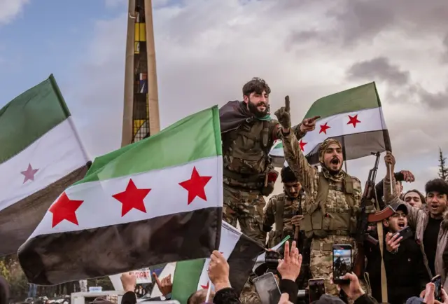 Suriye bayrakları sallayan kamuflaj giysili ve silahlı kişiler