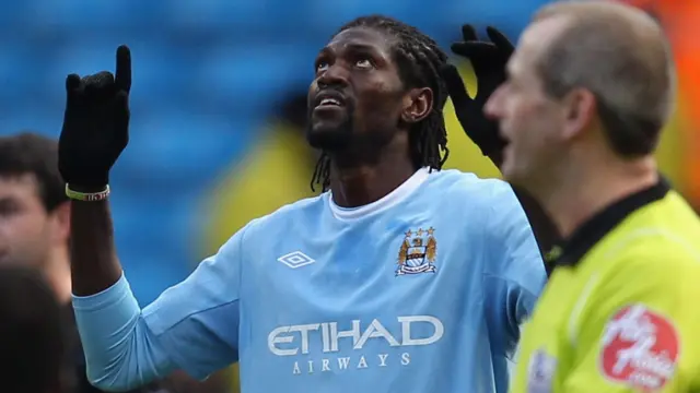 Emmanuel Adebayor, vêtu d'un maillot bleu clair de Manchester City et de gants noirs, lève les yeux et montre le ciel alors qu'il célèbre un but, tandis qu'un arbitre vêtu d'un maillot lumineux est vu hors champ au premier plan.
