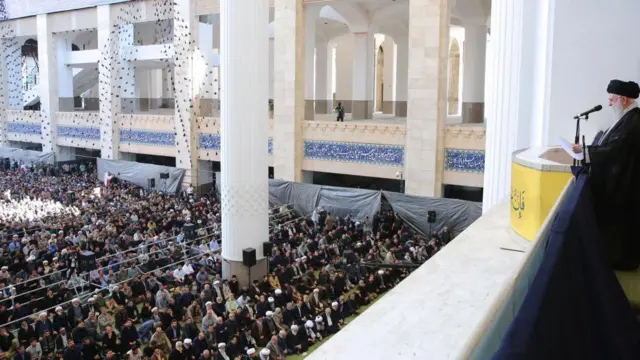 آیتالله علی خامنهای، رهبر ایران، در حالی که سلاحی در دست دارد، نماز جمعه را در مصلای امام خمینی تهران در اکتوبر ۲۰۲۴ امامت میکند.