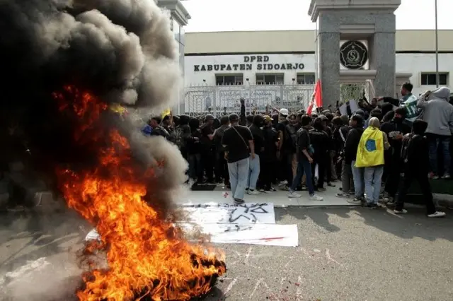 Pengunjuk rasa membakar ban saat menggelar aksi menolak UU TNI di depan Gedung DPRD Sidoarjo, Jawa Timur, Selasa (25/03).