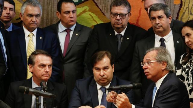 Bolsonaro, Maia e Guedes aparecem sentados em mesa e observados por outras pessoas durante apresentação da proposta da reforma da Previdência para militares
