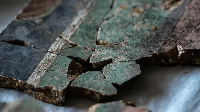 Una imagen de cerca de al menos 10 fragmentos de yeso que han sido unidos. En el lado derecho de la imagen se encuentra la sección rosa, luego una delgada línea divisoria negra y una banda verde pálido más gruesa. Hacia la izquierda de la imagen hay una fina línea divisoria blanca y luego una gruesa banda negra.