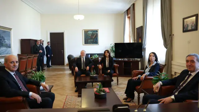 Beş siyasetçi u şeklinde koltuklarda oturmuşlar ve fotoğrafçıya bakıyorlar. Ortam son derece resmi.