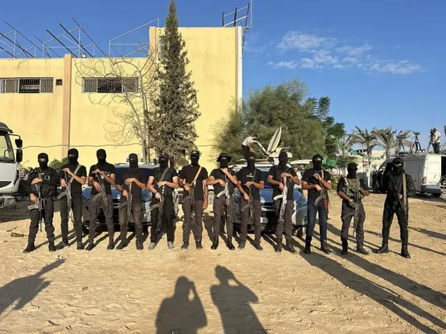 قوات أمن تابعة لحماس تنتشر في خان يونس في 13 أكتوبر/تشرين الأول 2025 مع اكتمال الاستعدادات في مستشفى ناصر لاستقبال الفلسطينيين الذين كانوا سيُطلق سراحهم بموجب اتفاق وقف إطلاق النار وتبادل الرهائن والسجناء بين إسرائيل وحماس. ويظهر في الصورة مسلحون يصطفون ويرتدون سترات سوداء ووجوههم ملثمة، بينما يحملون سلاحاً نارياً.