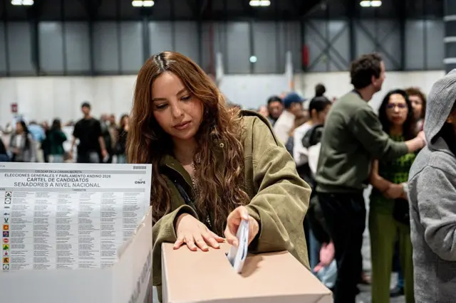 Una mujer deposita su voto en una urna en Madrid, España. Hay otras personas a su alrededor. 
