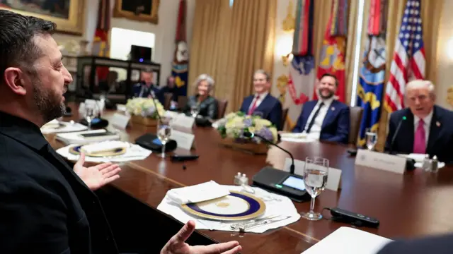 Zelenskiy, Beyaz Saray'da düzenlenen yemekte Trump ve ekibi ile bir araya geldi. Masada tabak ve bardakların yanı sıra mikrofonlar var ve herkes gülümsüyor.