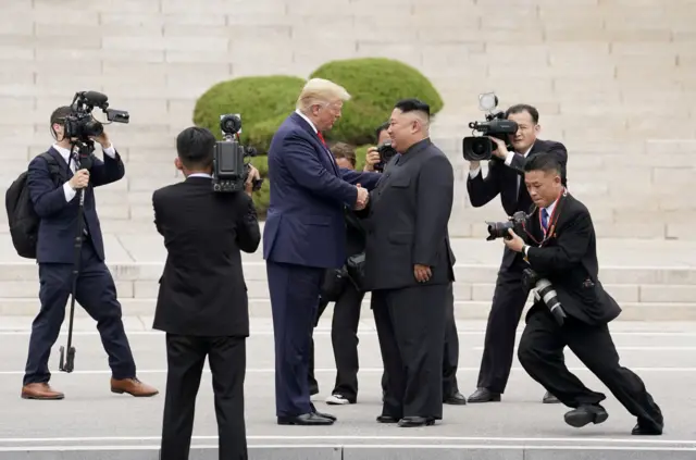 도널드 트럼프 미국 대통령과 김정은 북한 국무위원장이 판문점에서 악수하고 있다. 주변에는 양국 취재진이 두 정상의 만남을 촬영하고 있다.