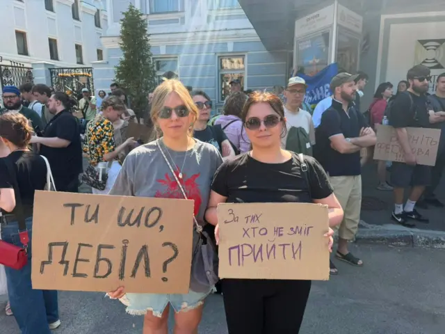 Две демонстранткиње у Кијеву држе транспаренте на којима пише: „Шта радиш, идиоте?“ и „Ово је за све оне који нису могли да буду овде“