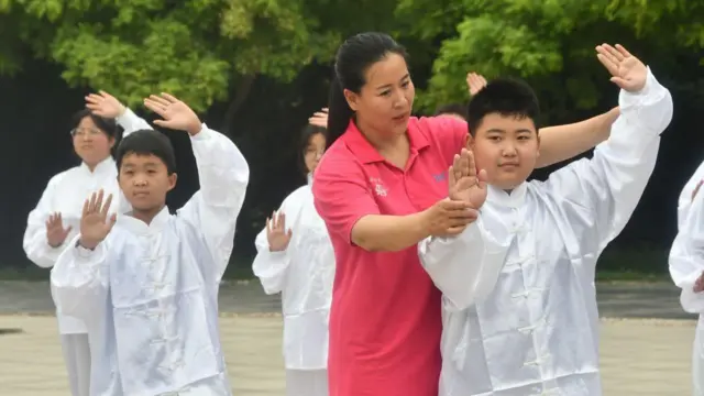 Una porfesora vestida de rojo enseña Tai Chi a niños vestidos de blanco