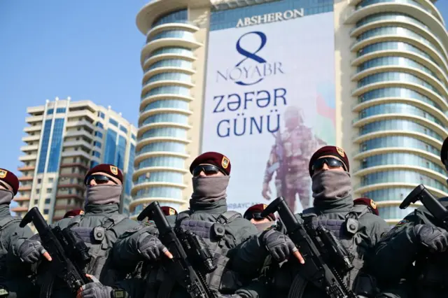 Военные в солнечный день в солнцезащитных очках на главной площади в Баку под плакатом «8 ноября — День победы»