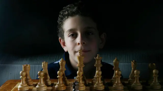 Хлопчик сидить за шаховою дошкою та посміхається