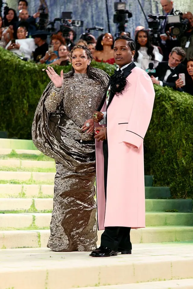 Rihanna vücudunu saran gümüş rengi bir elbise giyerken, A$AP Rocky uzun, açık pembe bir palto giymiş.