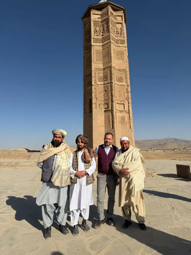 سفیر ترکیه با چند نفر از افراد طالبان که در طرفش ایستاده وی یکی از منارهای دوران سلطان محمود پشت سر او قرار دارد