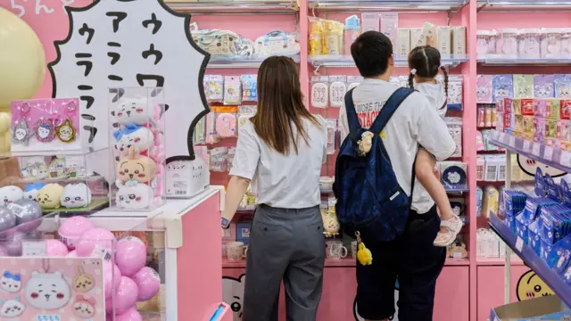 东京某卡通人物主题店内，一对父母带着年幼女儿选购玩具。父亲（中）右手抱着女儿。