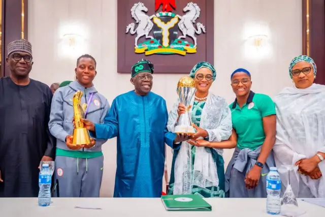 President Bola Tinubu receive Wafcon and best goalkeeper trophy from Super Eagles captain Rasheedat Ajibade and vice captain Chiamaka Nnadozie.