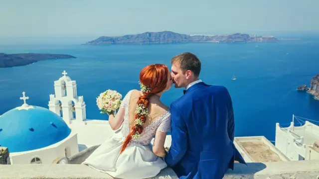 Wedding couple sidon dey watch di sea next to a church