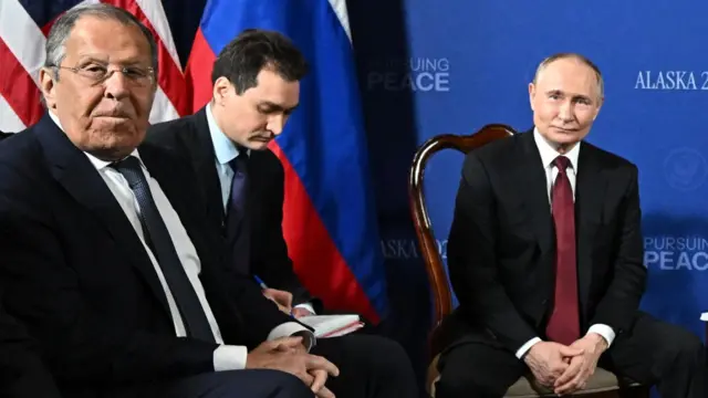 Сергей Лавров (в деловом костюме), переводчик с блокнотом и Владимир Путин, слушающий вопросы репортеров перед встречей с Дональдом Трампом