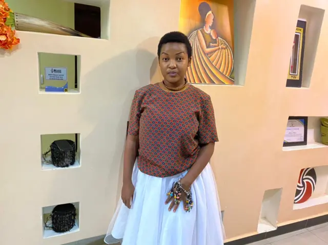 Clarisse Karasira ahagaze mu nzu akoreramo ibijyanye n'ubuhanzi bwe