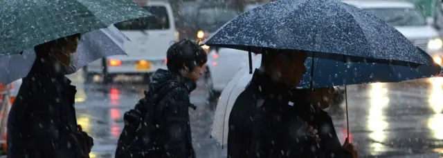 Pedestrians are heading to work in snowfall during the early morning hours in Tokyo on November 24, 2016