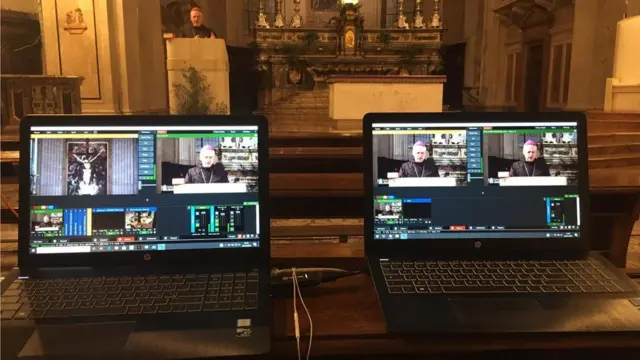 Dois laptops com tela mostrando transmissãovbet resultsvídeo, com padre no altar ao fundo