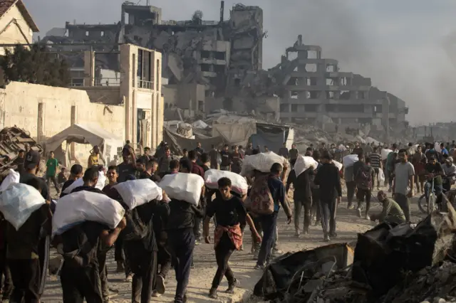 نازحون فلسطينيون يحملون مواد إغاثية على طول شارع الرشيد، غرب جباليا، 22 يونيو/حزيران 2025