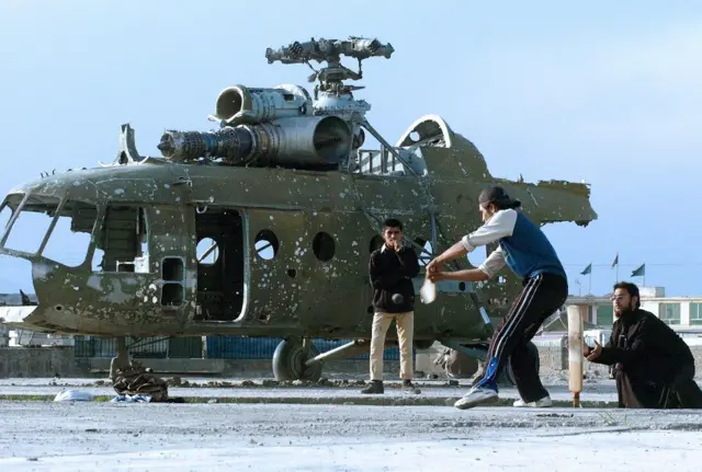 काबुल में एक दुर्घटनाग्रस्त हेलीकॉप्टर की पृष्ठभूमि में क्रिकेट खेलते बच्चों की फाइल फोटो, तस्वीर साल 2006 की है