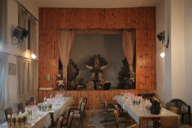 Sala doma kulture u Baništu spremna je za doček gostiju. Kako se termini početka obeležavanja Surve razlikuju od sela do sela, običaj je da grupe survakara iz jednog mesta posećuju druga kao gosti i zajedno sa domaćinima učestvuju u ceremoniji. Maske koje se ovde čuvaju tokom godine izložene su na bini.