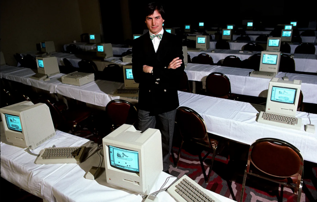 Steve Jobsaposta rejeitada esporte da sortebraços cruzados com olhar confiante entre mesas com computadores Macintosh