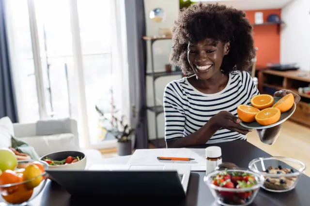 Une nutritionniste joyeuse et diversifiée montre à sa cliente, lors d'un rendez-vous virtuel, des fruits et légumes sains, des compléments alimentaires et des suppléments vitaminiques destinés à la santé et à l'alimentation.