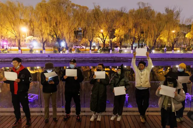 People gather for a vigil and hold white sheets of paper in protest over coronavirus disease (COVID-19) restrictions, during a commemoration of the victims of a fire in Urumqi, as outbreaks of COVID-19 continue, in Beijing