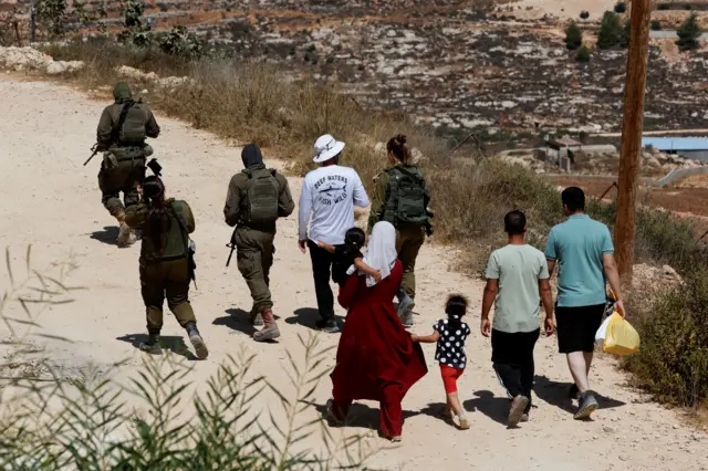 الفلسطيني الأمريكي لؤي أبو ريدة يسير برفقة أفراد من الجيش الإسرائيلي وجاريه رقية ويوسف حسن قرب منزله في قرية قصرة بالضفة الغربية المحتلة، بعد تمكنه من الوصول إليه، 19 أغسطس/آب 2026. وكان مستوطنون إسرائيليون قد طوقوا المنزل لأكثر من أسبوع.