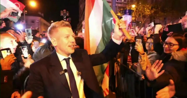 Peter Magyar onde sonriente una bandera de Hungría rodeado de seguidores en la celebración de su triunfo electoral en Budapest.
