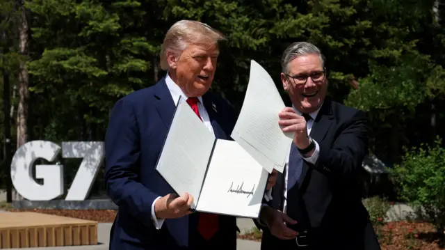 Дональд Трамп и Кир Стармер держат в руказ подписанный документ на фоне больших букв G7.