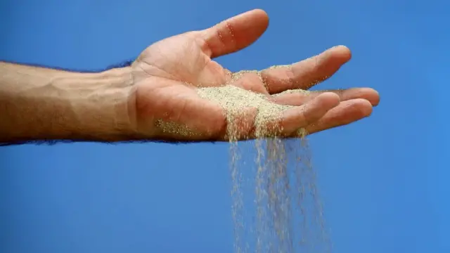 Mano con arena corriendo entre los dedos