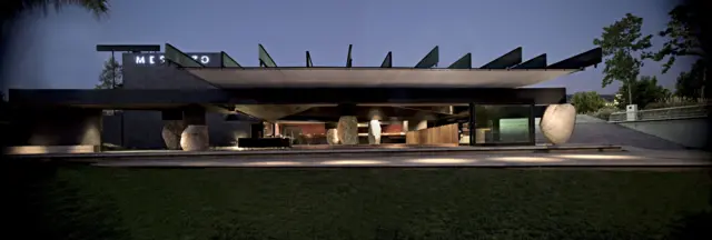 Fachada nocturna de un edificio moderno con techo plano, grandes volúmenes de piedra y una iluminación cálida que resalta sus líneas horizontales.