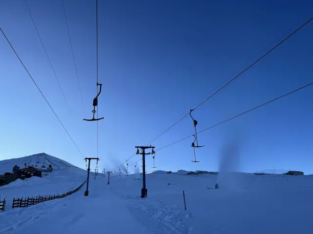 Teleférico em estação de esqui, com 'fumaças' de canhões de neve