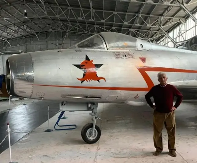 মিগ-২১ এর সামনে লাল সোয়েটার পরে দাঁড়িয়ে আছেন বয়সী মি. জয়াল 