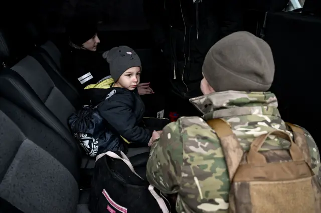 Một nữ quân nhân trò chuyện với một cậu bé nhỏ — người được các sĩ quan cảnh sát của Phòng Cảnh sát Quận Huliaipole thuộc Vùng Zaporizhzhia sơ tán khỏi ngôi làng tiền tuyến Vozdvyzhivka ở huyện Polohy, cùng với mẹ em là Anna và hai người anh em — trên chiếc xe tải của các tình nguyện viên khi gia đình chuẩn bị tiếp tục hành trình đến nơi an toàn, tại vùng Zaporizhzhia, Ukraine, ngày 19 tháng 11 năm 2025. (Ảnh: Dmytro Smolienko/Ukrinform) KHÔNG SỬ DỤNG CHO NGA. KHÔNG SỬ DỤNG CHO BELARUS. (Ảnh: Ukrinform/NurPhoto qua Getty Images)