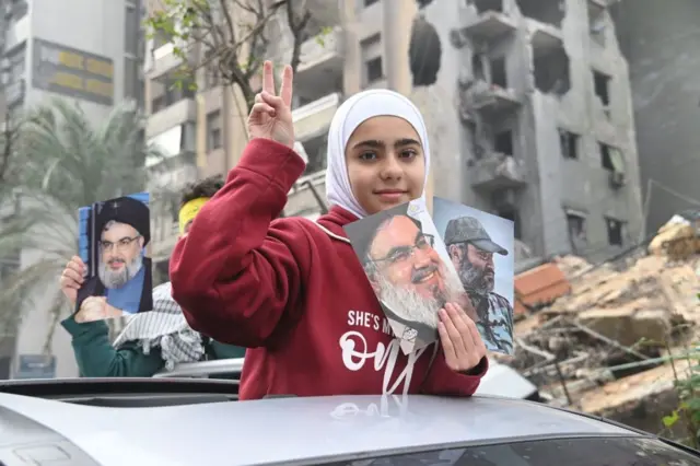 دختر محجبه لبنانی دستش را به‌ علامت پیروزی بالا برده، با عکسی از رهبر پیشین حزب‌الله در دست