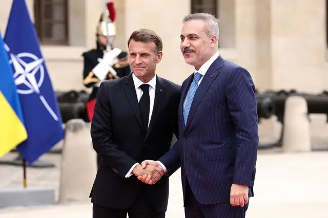 Hakan Fidan ve Fransa Cumhurbaşkanı Emmanuel Macron el sıkışıyor.