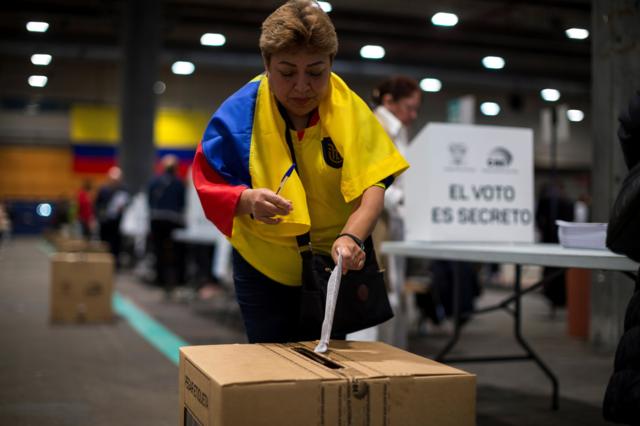 Una ecuatoriana vota envuelta en la bandera de su país en la consulta popular promovida por el presidente Noboa