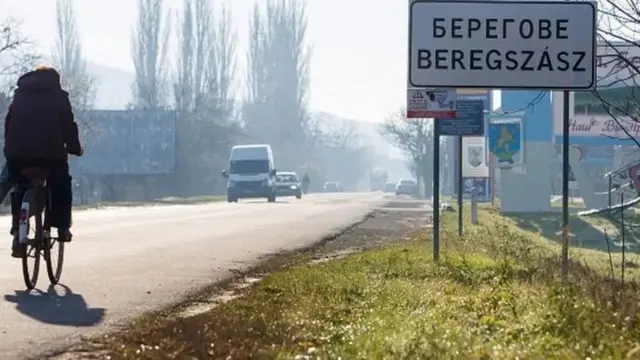 Найбільше угорців живе у Берегівському районі Закарпатської області. Дорожній знак українською і угорською мовами "Берегове", біля якого проїздить на велосипеді жінка.