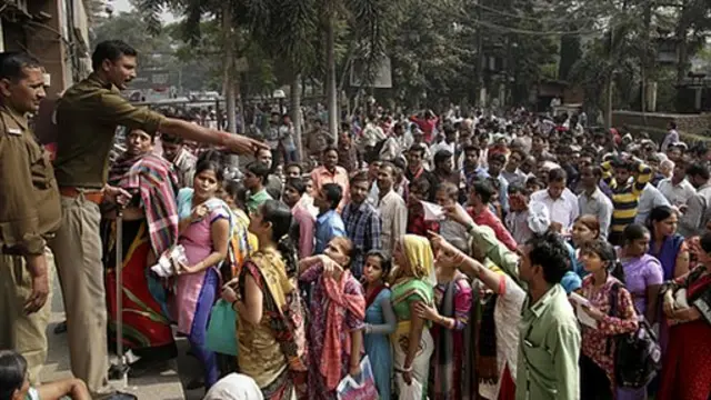 Un policía intenta calmara a la gente haciendo fila frente a un banco en Delhi