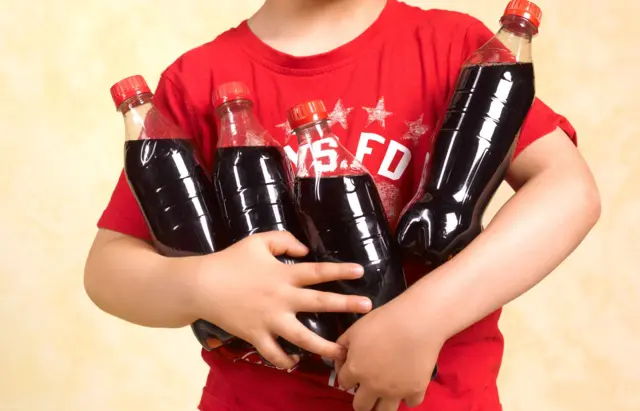 सॉफ्ट ड्रिंक्सच्या बाटल्या घेतलेला लहान मुलगा