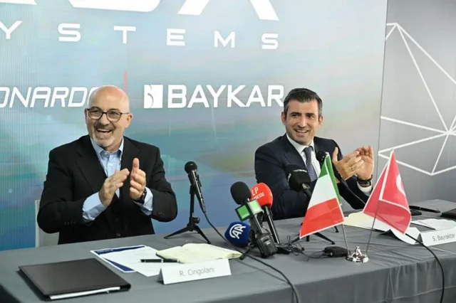Leonardo CEO'su Roberto Cingolani (solda) ve Baykar Yönetim Kurulu Başkanı Selçuk Bayraktar (sağda) alkışa katılıyor. İkisi de gülümsüyor.