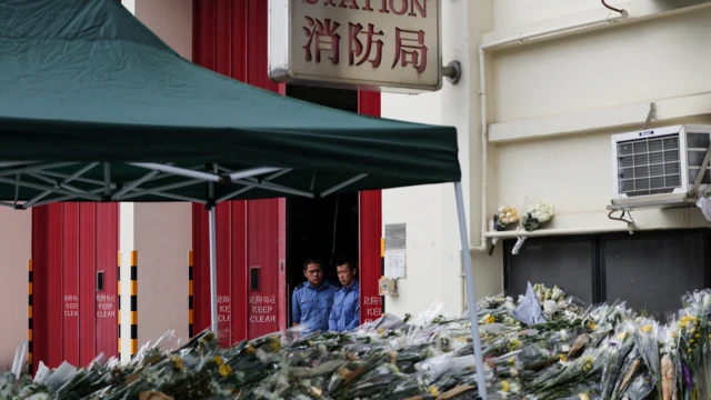 在沙田消防局入口處，消防員們正在哀悼，人們繼續獻花悼念在太埔宏福苑火災中殉職的消防員何偉豪。