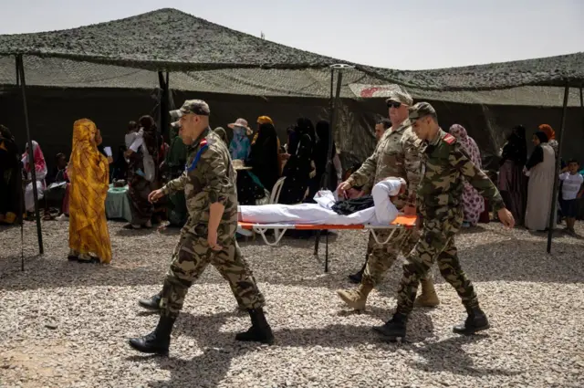 Des militaires américains tiennent un brancard sur lequel est couchée une personne vêtue de blanc